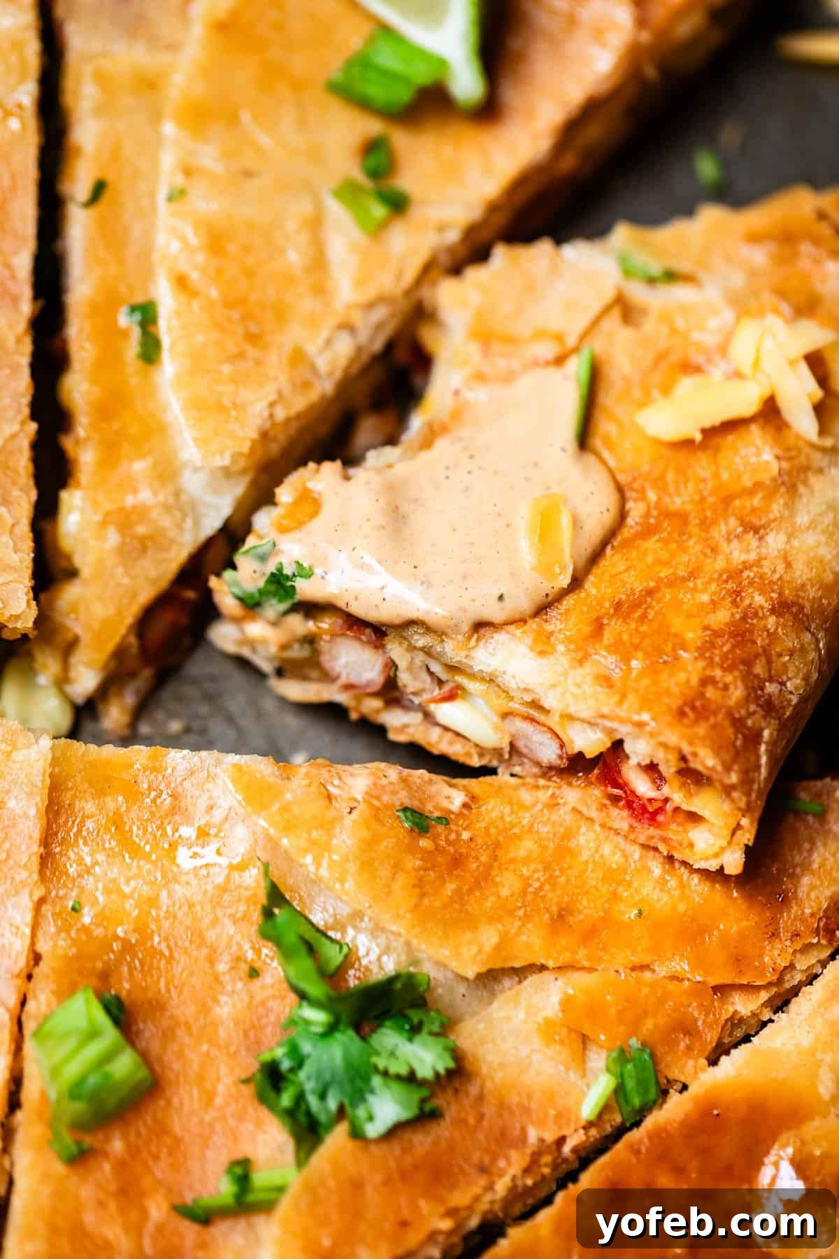 Crispy Sheet Pan Chicken Quesadillas 17 Close-up of golden, crispy quesadilla slices filled with beans and vegetables, topped with creamy sauce, melted cheese, and garnished with cilantro.
