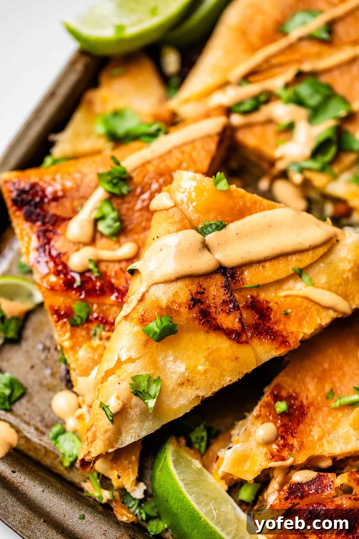 Crispy Sheet Pan Chicken Quesadillas 18 Close-up of crispy quesadilla triangles topped with chopped cilantro and a drizzle of creamy sauce, with lime wedges on the side.