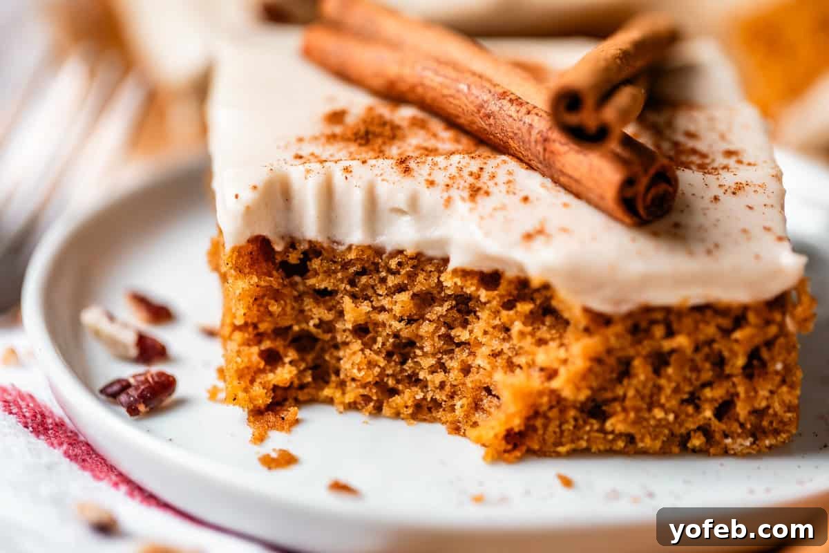 Autumn Spiced Pumpkin Sheet Cake with Maple Cream Cheese Frosting 3 A close-up of a slice of spiced cake topped with white frosting and two cinnamon sticks on a white plate, with crumbs and pecans scattered nearby, exuding warmth and coziness.