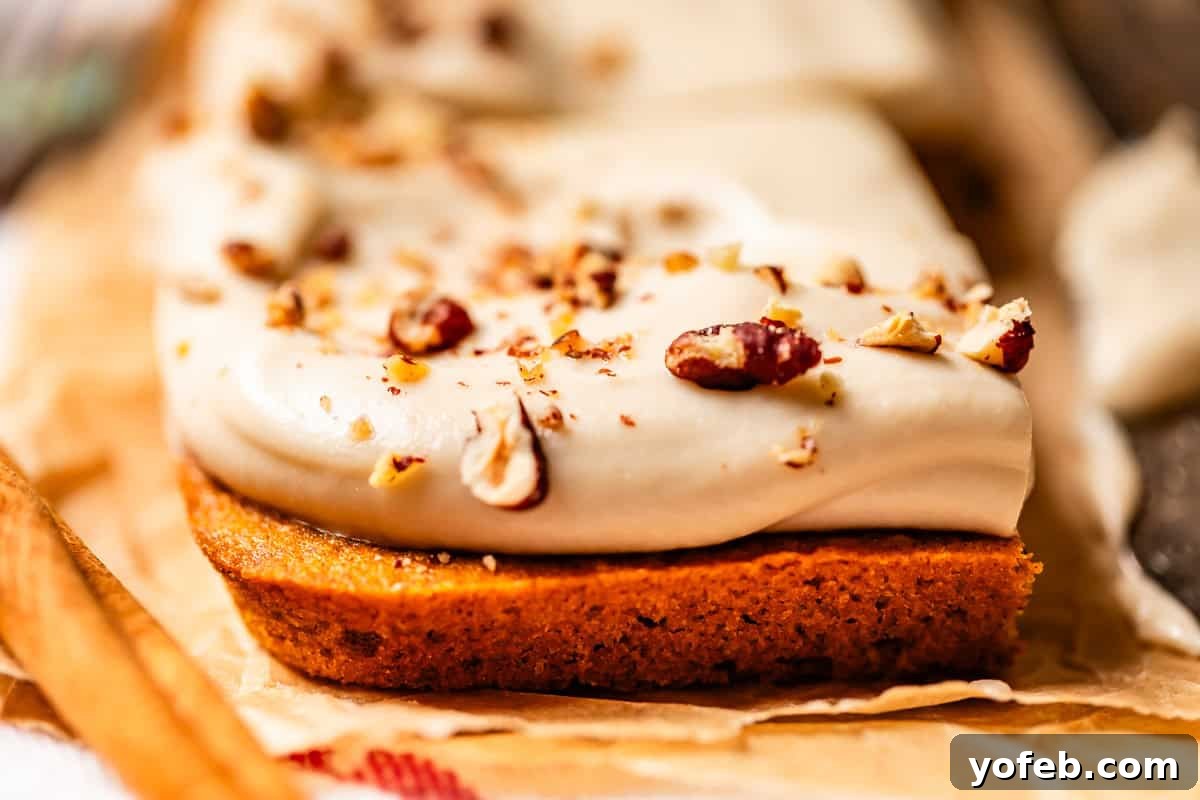 Autumn Spiced Pumpkin Sheet Cake with Maple Cream Cheese Frosting 6 A close-up of a frosted bar dessert topped with chopped nuts on parchment paper. The thick, creamy frosting is spread over a golden-brown base, with nut pieces sprinkled on top, showcasing a perfect frosting-to-cake balance.