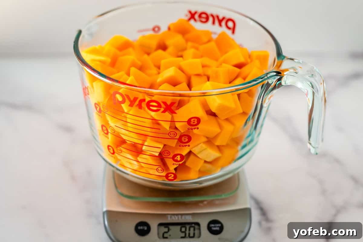 Conquer Butternut Squash: A Simple Guide to Safe Slicing 15 A transparent glass Pyrex measuring cup, filled to the brim with vibrant orange diced butternut squash, is positioned on a digital kitchen scale, which displays a precise weight of 2.90 pounds. The measuring cup clearly shows volume markings up to 8 cups.