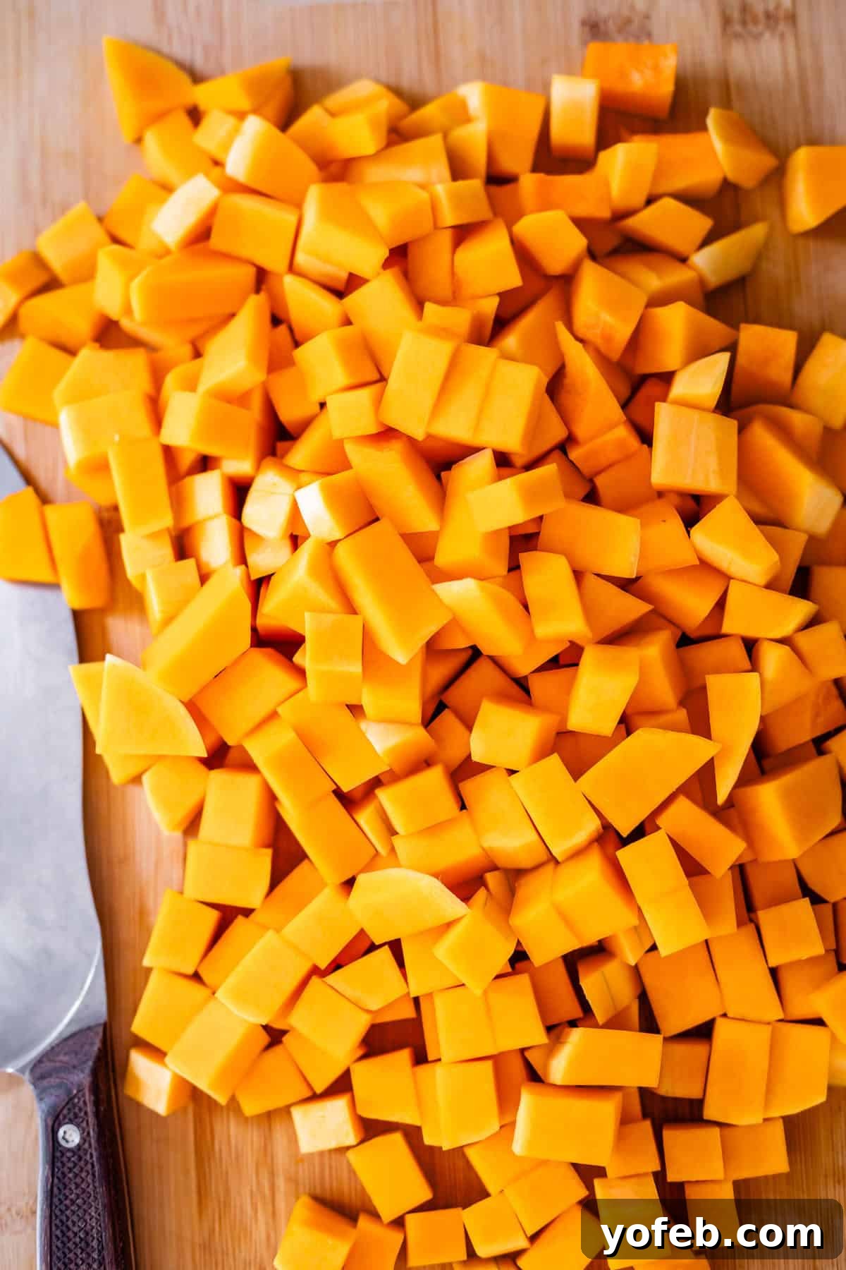 Conquer Butternut Squash: A Simple Guide to Safe Slicing 4 Perfectly diced, vibrant orange butternut squash cubes neatly arranged on a wooden cutting board, with a professional chef’s knife with a dark handle resting beside them, illustrating a successful preparation.