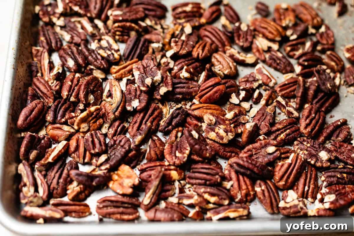 Buttery Pecan Bliss 8 A baking tray filled with roasted pecan halves and pieces, spread out in a single layer. The nuts appear toasted and slightly seasoned.
