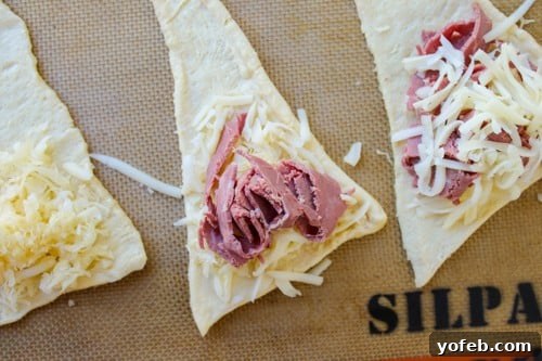 Layering cheese, sauerkraut, and corned beef on crescent roll dough