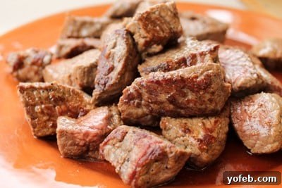 Hearty Slow-Simmered Beef Barley Soup 3 Chunks of perfectly browned beef stew meat on a plate, ready for adding to the slow cooker for Beef Barley Soup.