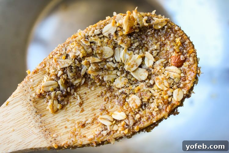 A wooden spoon stirring a mixture of oats, nuts, and maple syrup in a bowl, capturing the essence of homemade granola preparation.