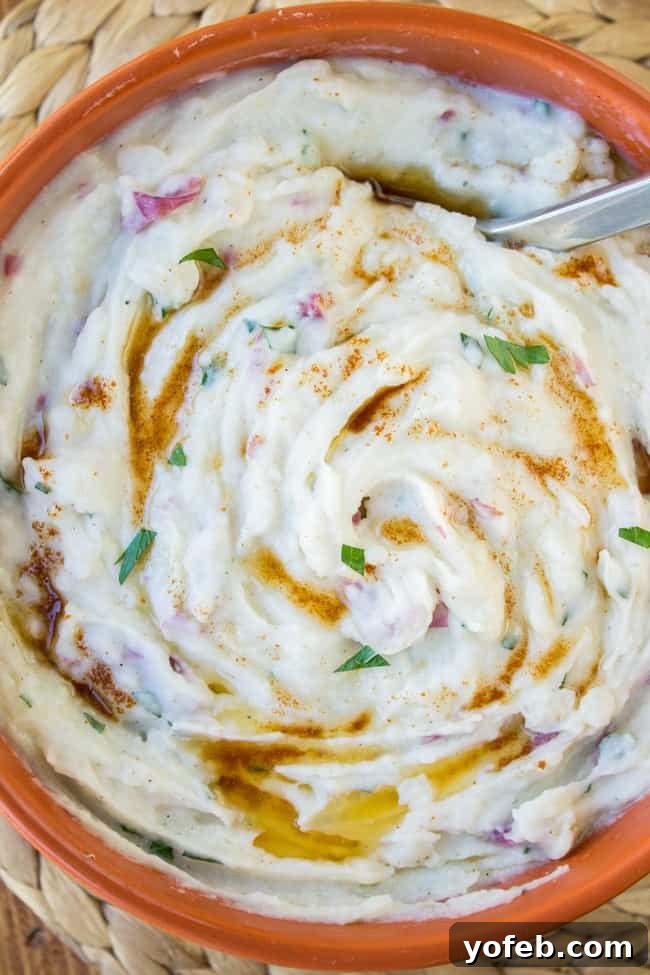 A bowl of creamy mashed potatoes garnished with paprika, fresh herbs, and a swirl of melted butter, with a spoon resting on the side.