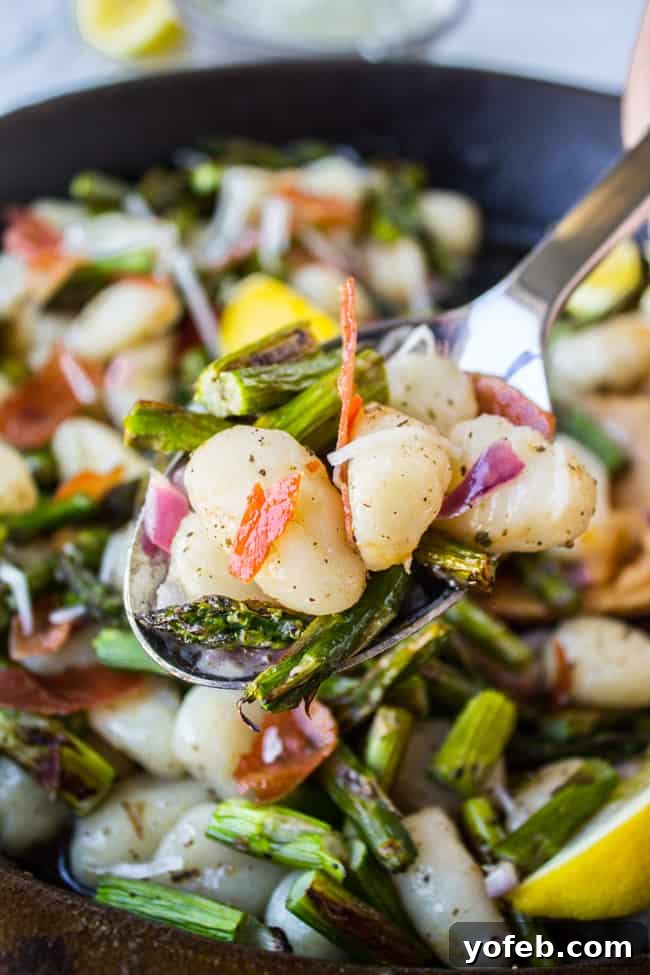 Nutty Brown Butter Gnocchi with Crisp Asparagus 5 A metal spoon lifting a forkful of gnocchi, asparagus, and prosciutto from a pan, glistening with brown butter sauce.