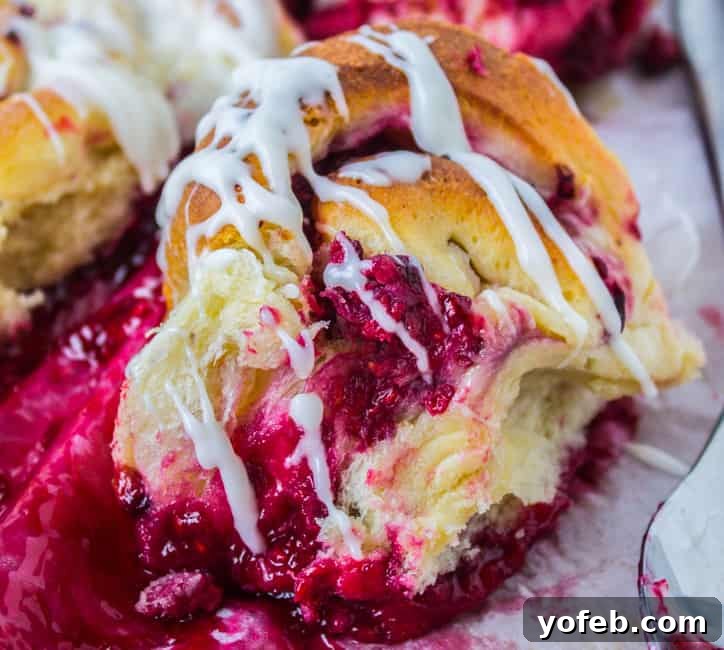 A close-up of a raspberry sweet roll, showing the fluffy dough and raspberry swirls, glistening with frosting.