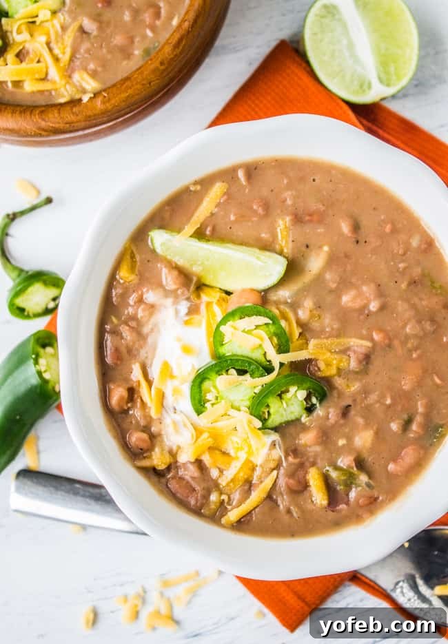 Classic Tejano Slow Cooker Frijoles 3 overhead shot of a bowl of Mexican pinto beans garnished with lime, cheddar, and sour cream.