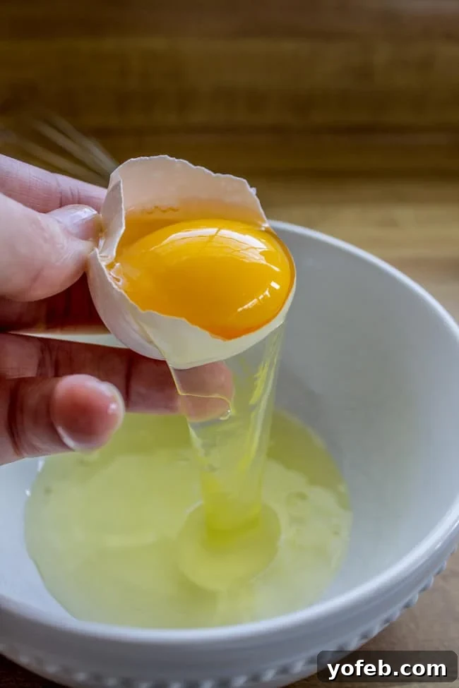 Extra egg yolk for ultimate chewiness. Hand separating an egg yolk from the white, a key step for chewy cookies.