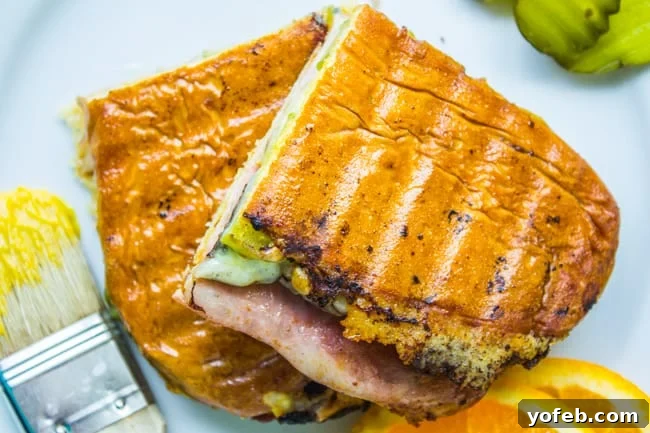 Pressed Perfection: The Ultimate Cubano 4 a Cuban sandwich cut in half with orange slices, pickles, and mustard nearby.