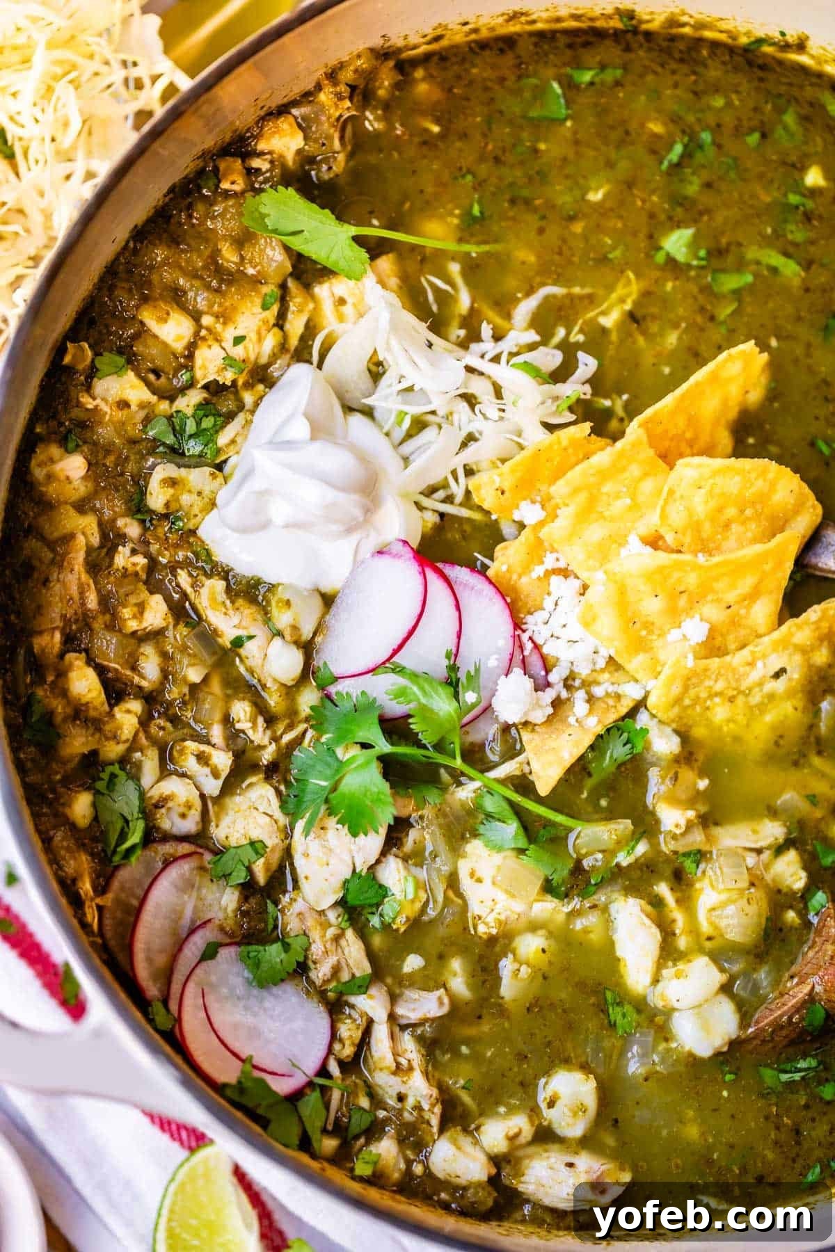 Vibrant Green Chicken Pozole in Minutes 4 A bowl of green pozole soup garnished with sliced radishes, fresh cilantro, tortilla chips, shredded cheese, and a dollop of sour cream, with visible pieces of hominy and chicken in a vibrant green broth.