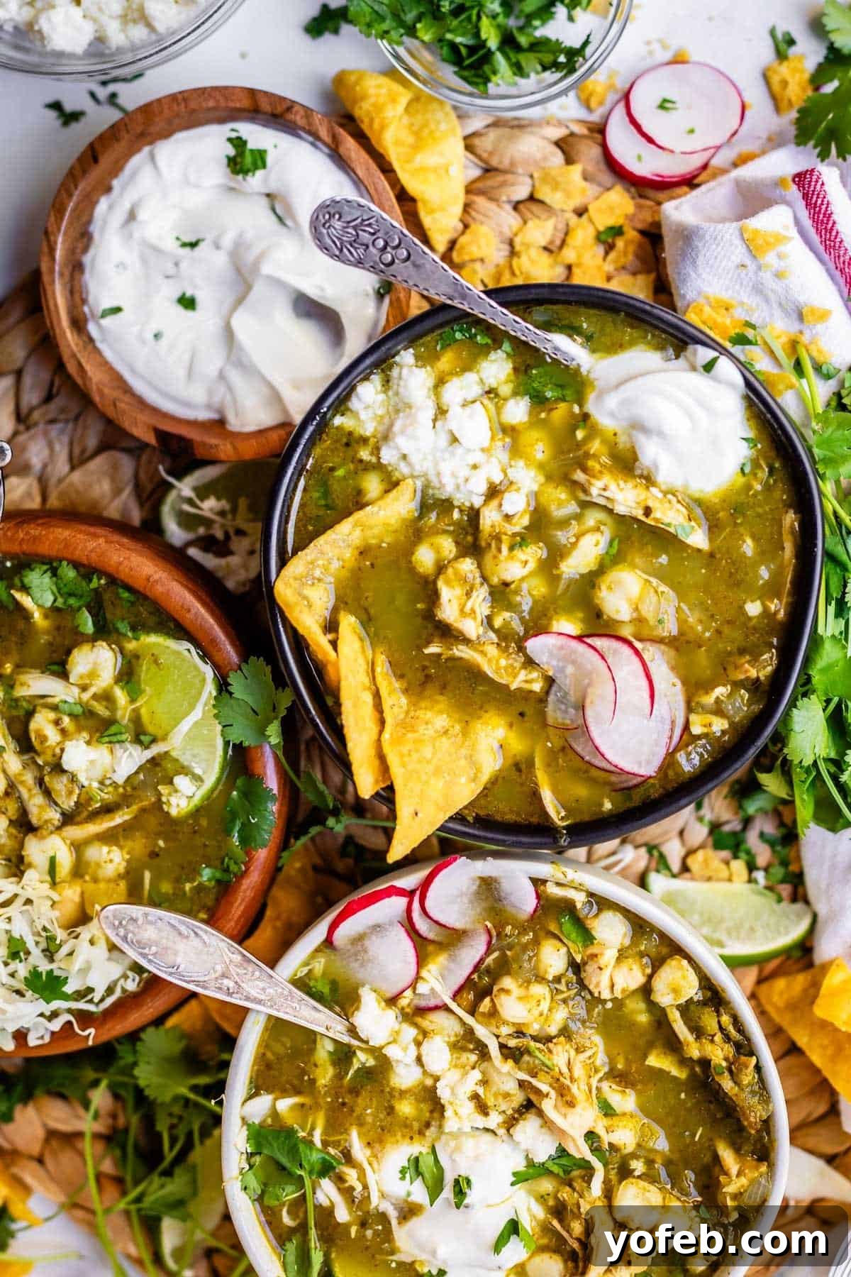 Vibrant Green Chicken Pozole in Minutes 5 Bowls of green chicken pozole topped with radish slices, tortilla chips, sour cream, and fresh cilantro, surrounded by lime wedges, corn chips, and additional garnishes on a textured surface.