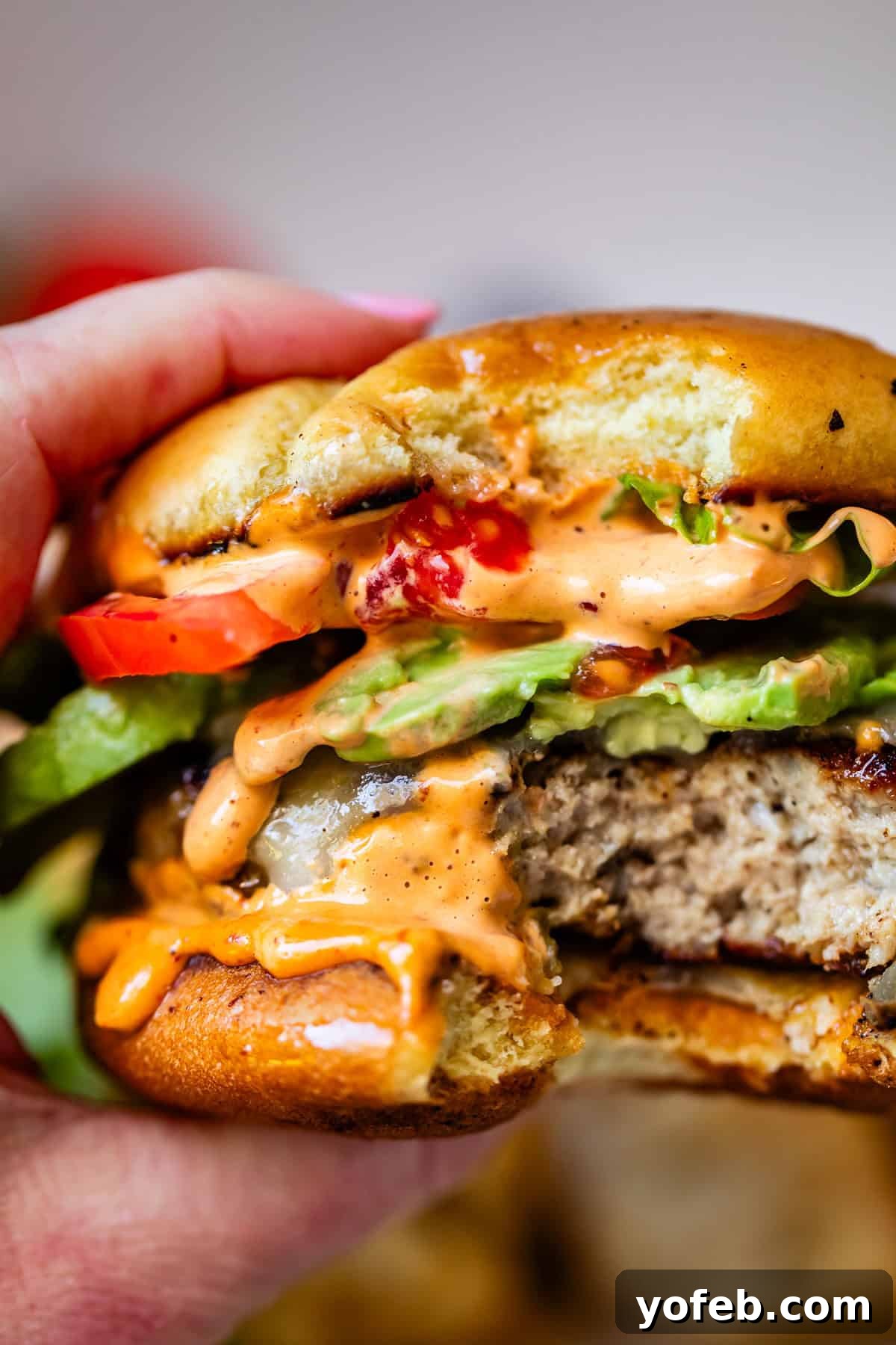 Game-Changing Turkey Burgers 16 A hand gently holds a bitten turkey burger, revealing its vibrant layers of crisp lettuce, ripe tomato, beautifully melted cheese, and a creamy sauce that drips tantalizingly. The juicy patty and perfectly toasted bun are clearly visible, emphasizing the lasting quality and deliciousness of the burger, even as a leftover meal.
