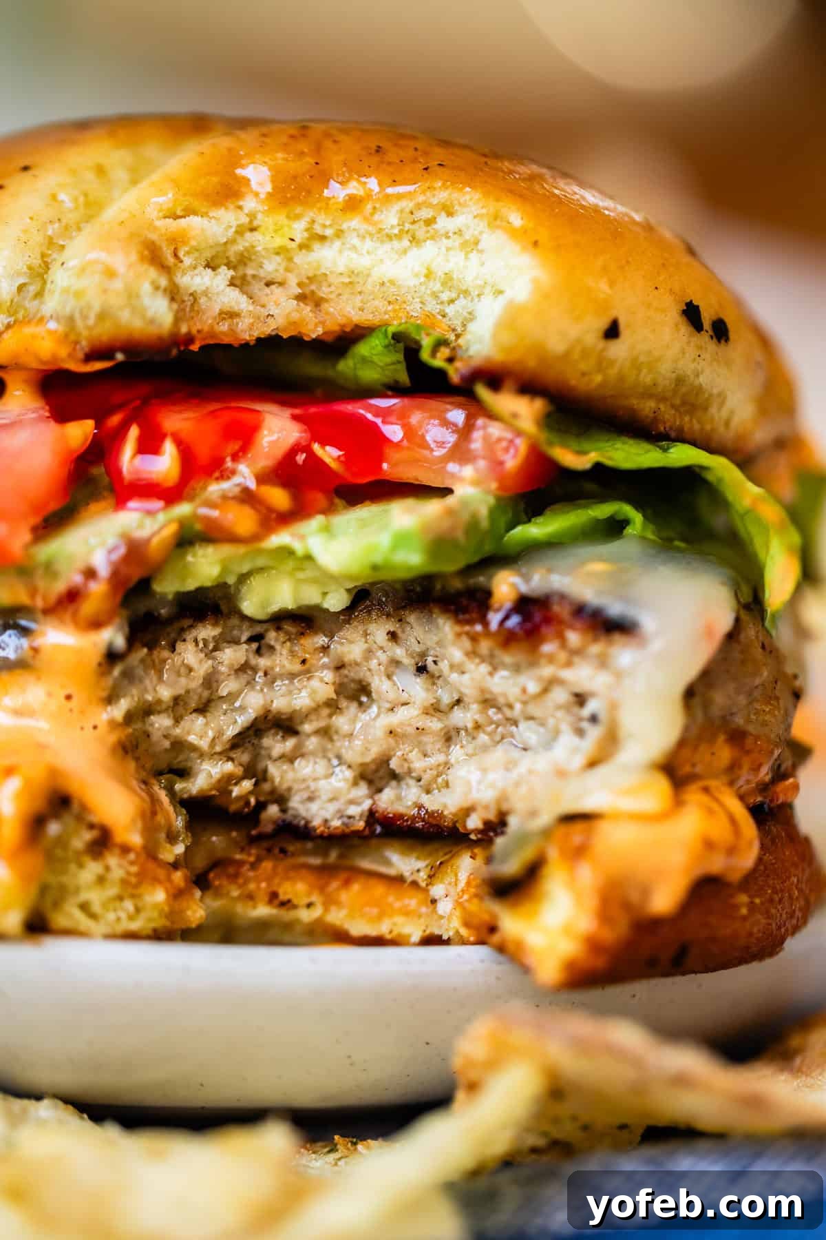 Game-Changing Turkey Burgers 4 A delectable close-up of a juicy cheeseburger with a perfect bite taken out, revealing layers of glistening melted cheese, crisp lettuce, ripe tomato, a generous dollop of creamy sauce, and a thick, flavorful turkey patty nestled within a golden, toasted bun. This photo undeniably highlights the irresistible appeal and succulence of the burger.