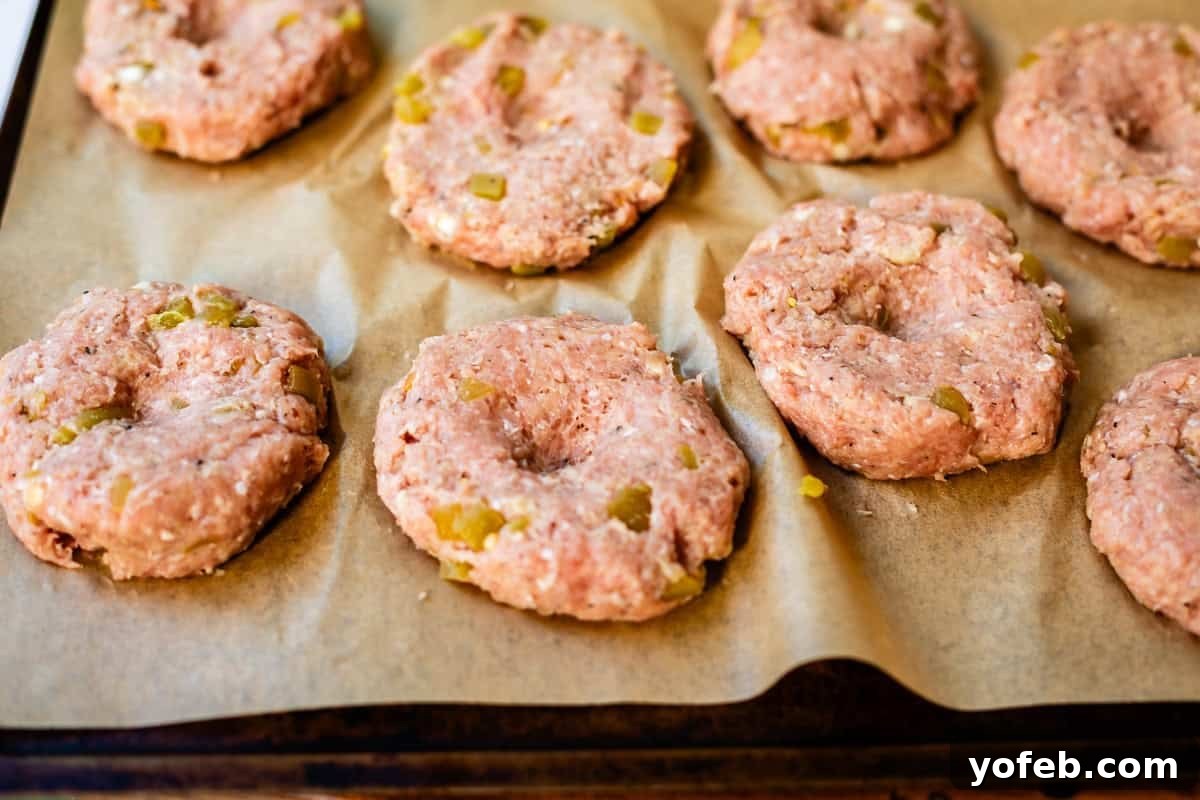 Game-Changing Turkey Burgers 9 Raw, perfectly seasoned ground turkey patties, subtly infused with finely chopped vegetables, are meticulously arranged on a baking sheet lined with parchment paper, poised and ready for cooking. Each patty distinctly features a small, expertly formed indentation in its center, a key preparation step.