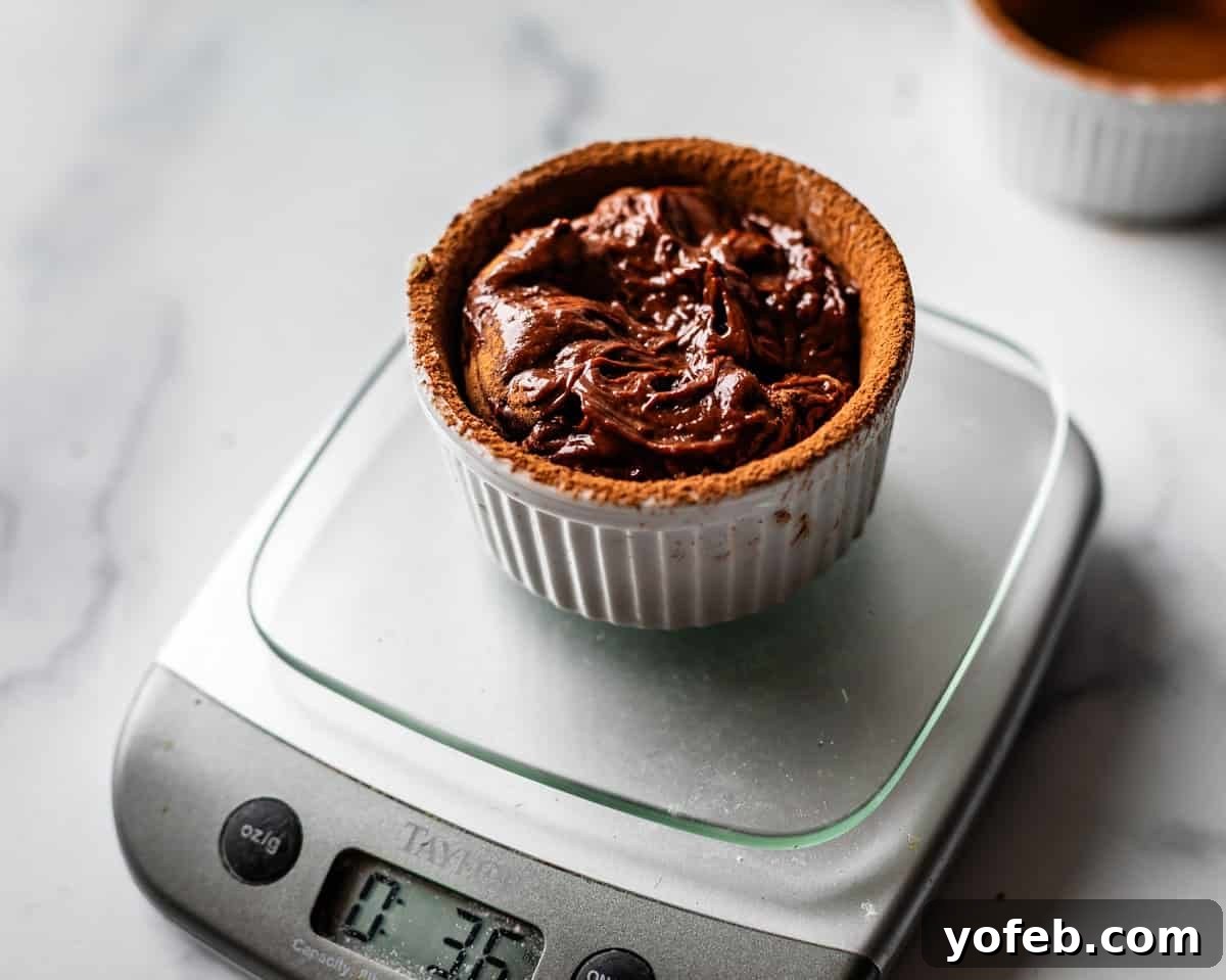 Molten Chocolate Magic 19 A small white ramekin filled with chocolate cake batter sits on a digital kitchen scale, displaying a weight of 3.5 ounces; another ramekin is blurred in the background on a white surface.