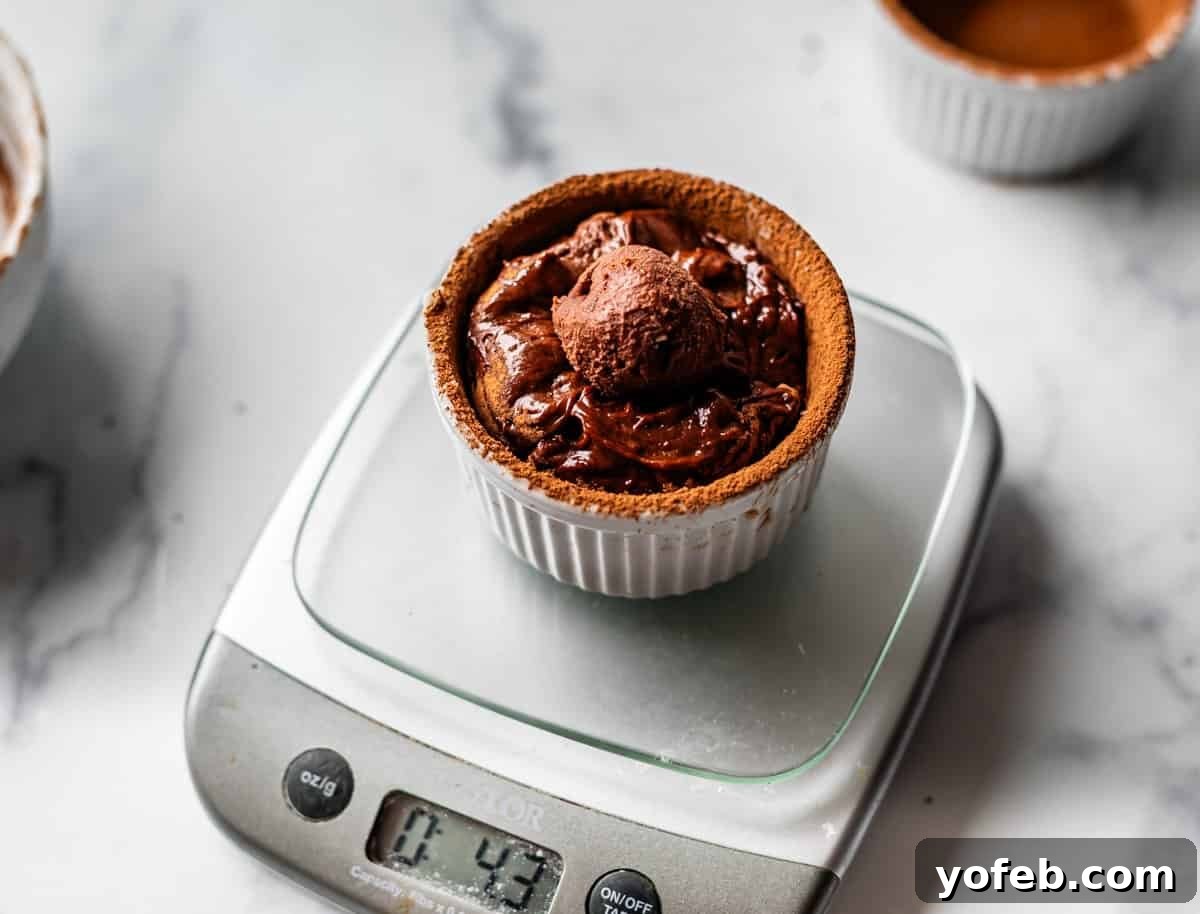 Molten Chocolate Magic 20 A chocolate soufflé in a white ramekin sits on a digital kitchen scale displaying 4.43 ounces, on a marble countertop. Another ramekin and a mixing bowl are partially visible in the background.