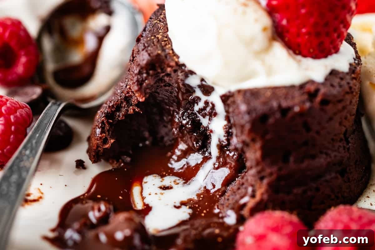 Molten Chocolate Magic 27 A close-up of a molten chocolate lava cake with a gooey chocolate center, topped with vanilla ice cream and a strawberry, surrounded by fresh raspberries and a spoon scooping the dessert.