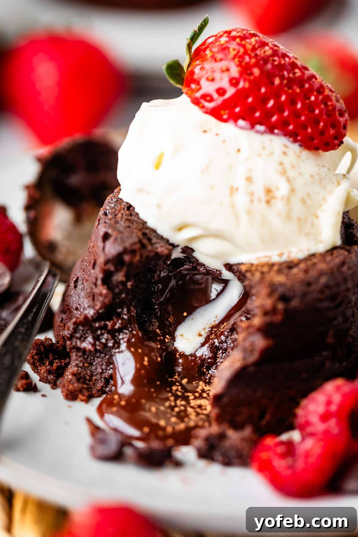 Molten Chocolate Magic 5 A close-up of a chocolate lava cake with melted chocolate oozing out, topped with a scoop of vanilla ice cream and a fresh strawberry, surrounded by more strawberries and raspberries on a plate.