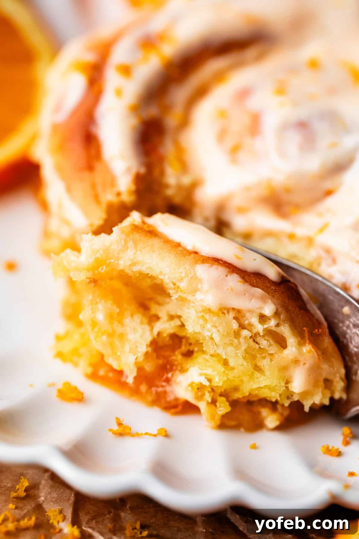 Zesty Orange Sweet Rolls 32 A close-up of a partially eaten orange sweet roll, lavishly topped with creamy icing and delicate orange zest. Served on a pristine white plate, the image clearly reveals the roll's soft, moist texture and vibrant citrus filling, inviting a closer look.