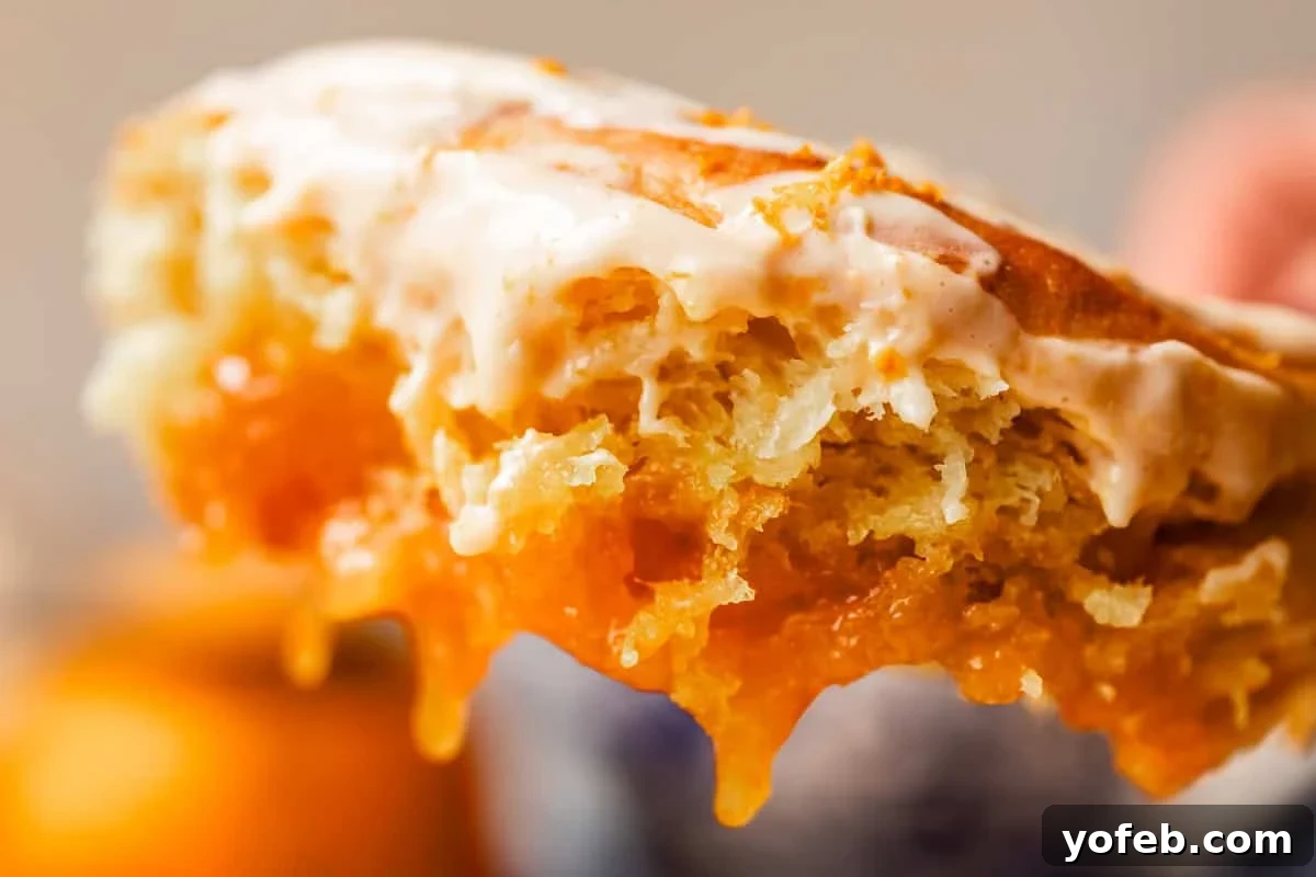 Zesty Orange Sweet Rolls 7 An enticing close-up of a flaky orange roll, revealing a luscious, gooey orange filling delicately oozing from its layers. The roll is artfully crowned with a smooth, creamy orange glaze, emphasizing its rich texture and decadent appearance. The background is softly blurred, ensuring the focus remains on the intricate details and appetizing appeal of this delightful dessert.