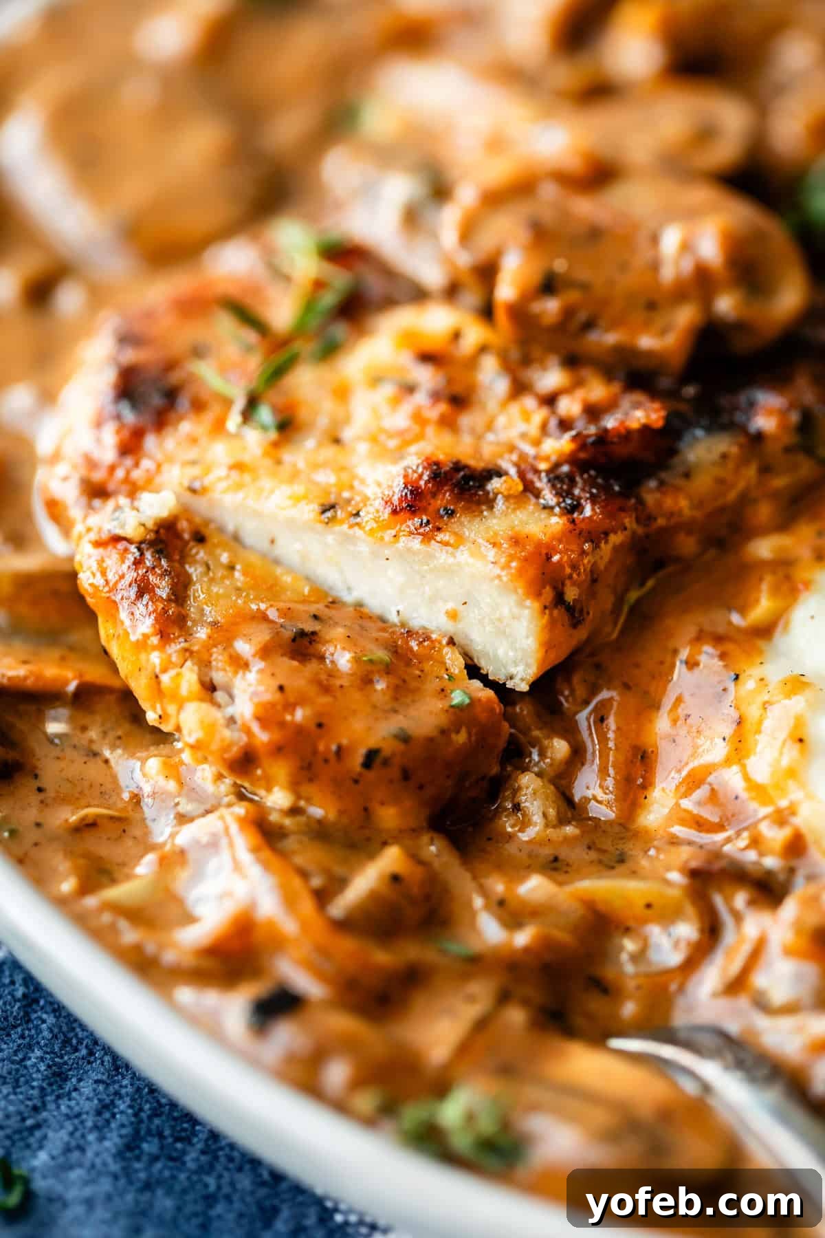 Tender Smothered Pork Chops 5 Close-up of a juicy, golden-brown chicken breast sliced in a creamy mushroom sauce, garnished with herbs. The sauce looks rich and flavorful, coating the chicken and mushrooms.