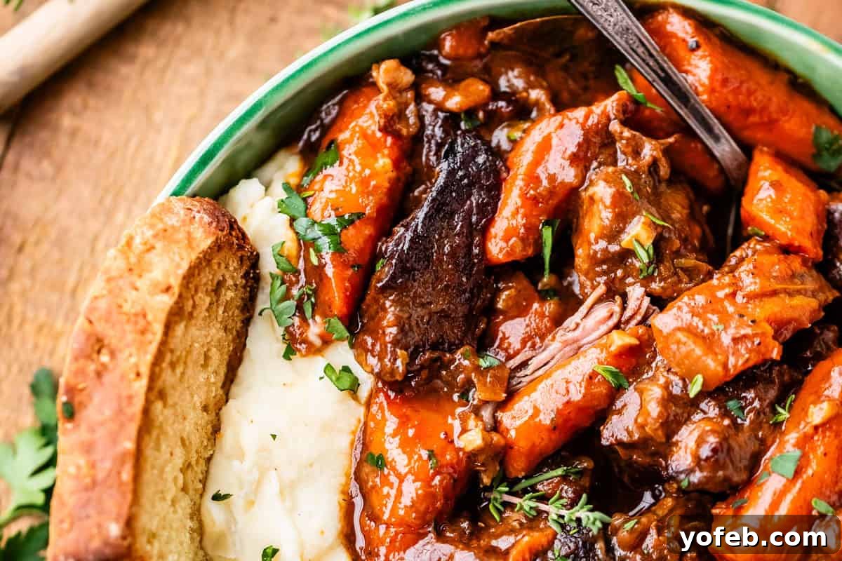 Hearty Irish Beef Stew 19 A close-up of a bowl filled with mashed potatoes and beef stew with carrots, garnished with fresh herbs and served with a slice of bread. A spoon is in the bowl.