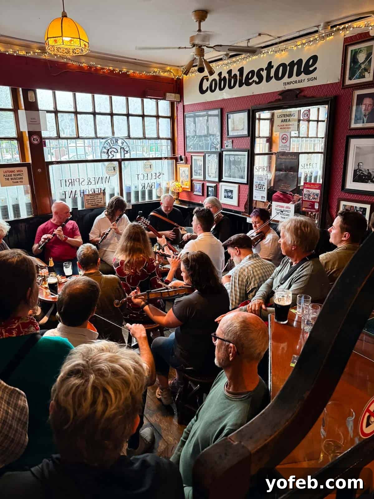 Hearty Irish Beef Stew 3 A lively group of musicians plays traditional Irish music in a cozy, crowded pub, surrounded by patrons enjoying drinks. The pub walls are decorated with framed photos and memorabilia, and a sign reads Cobblestone.