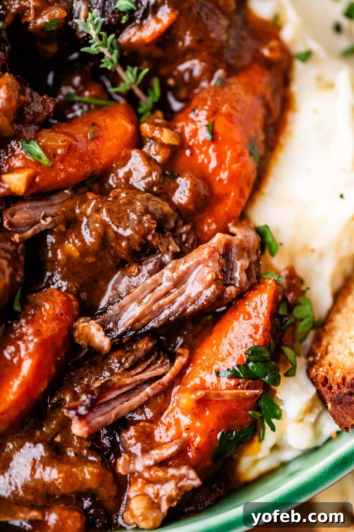 Hearty Irish Beef Stew 5 Close-up of tender pot roast with carrots and rich brown gravy, served over creamy mashed potatoes and garnished with fresh herbs. A piece of crusty bread is visible on the side.