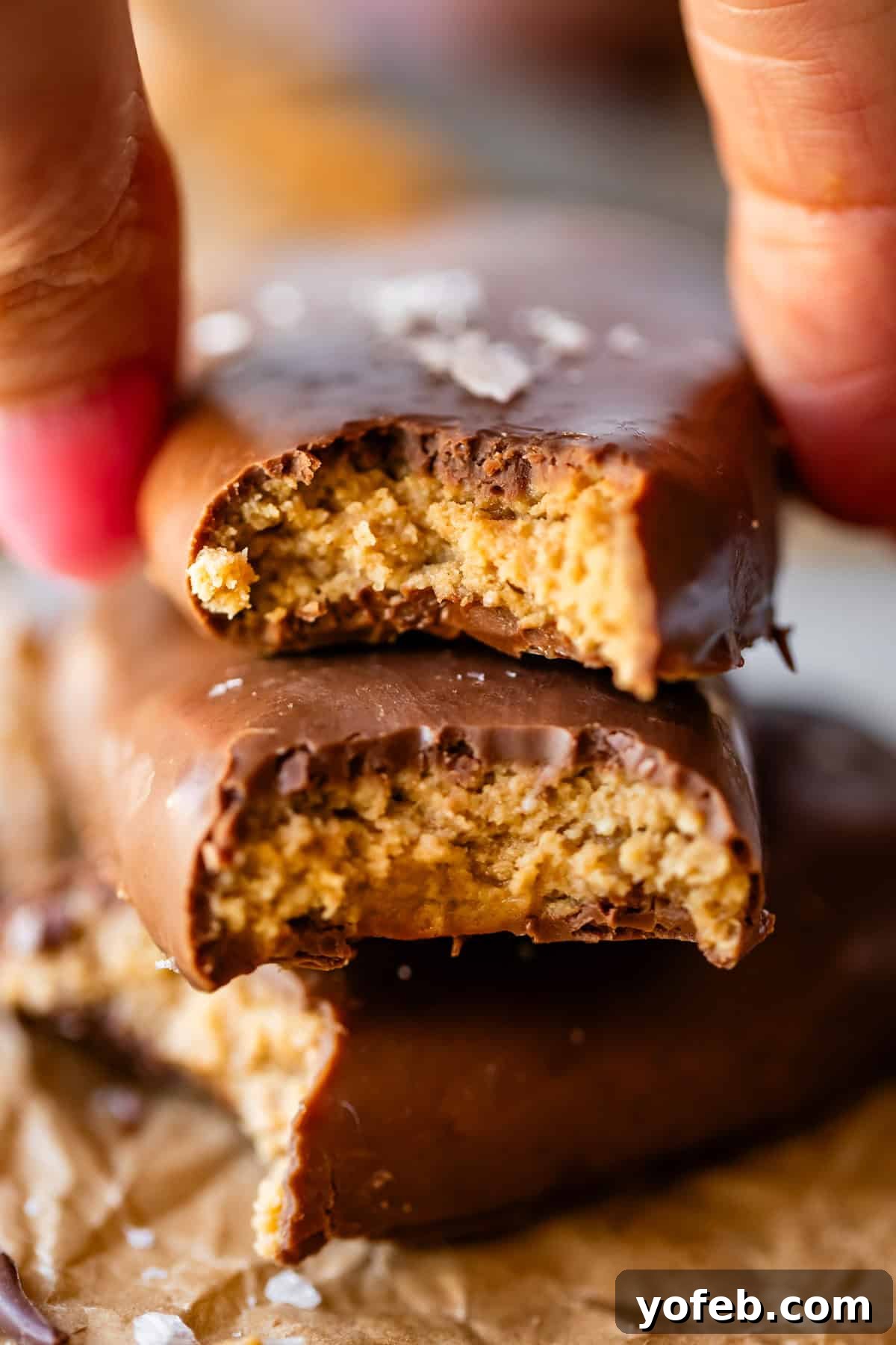 Reese's Easter Peanut Butter Bliss 23 A close-up of a hand holding a chocolate-coated peanut butter egg with a bite taken out, stacked on top of another partially eaten cookie, both showing a crumbly peanut butter filling.