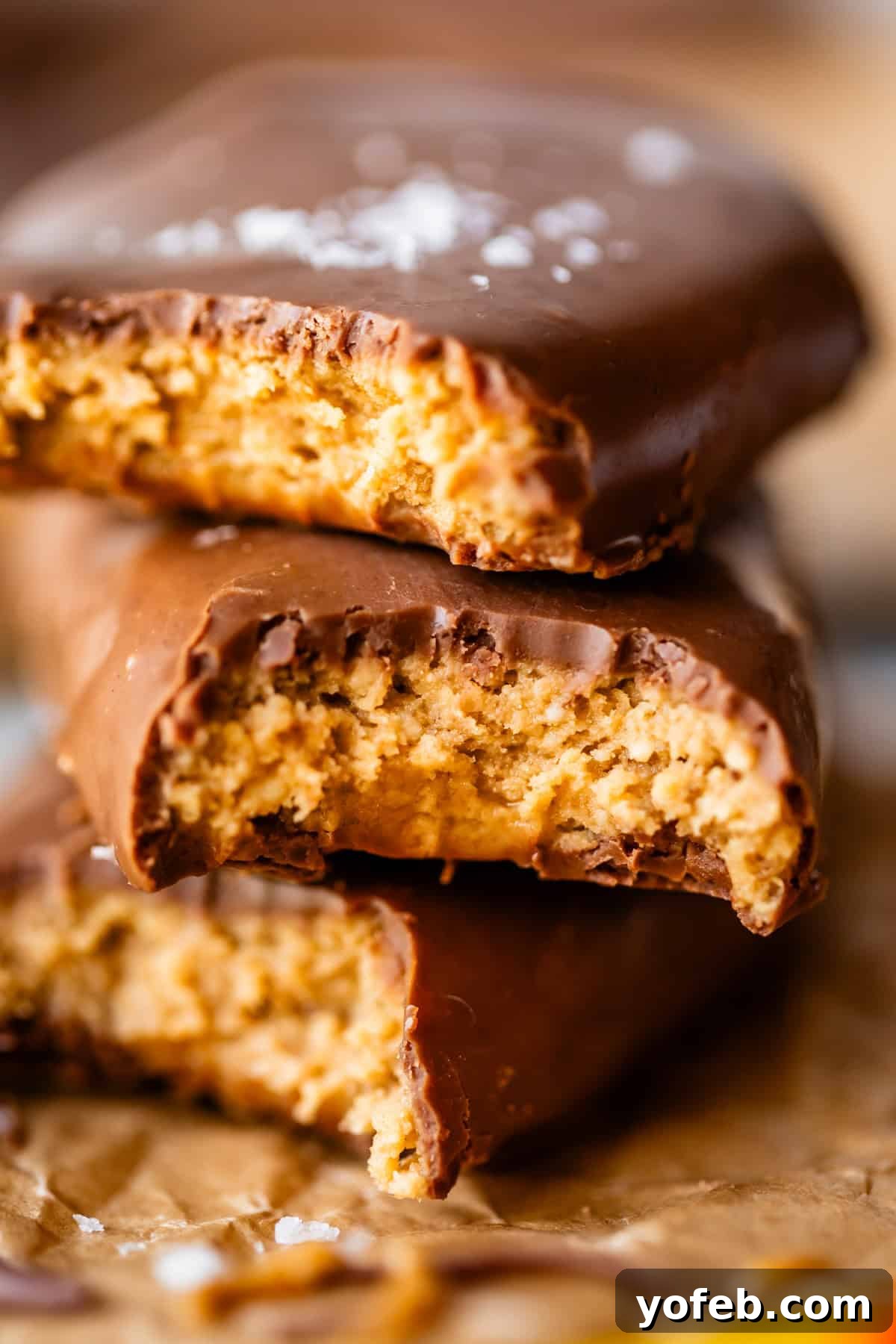 Reese's Easter Peanut Butter Bliss 4 Two chocolate-covered peanut butter eggs are stacked, both with large bites taken out, revealing a creamy peanut butter filling inside. The bars rest on a crumpled piece of brown parchment paper.