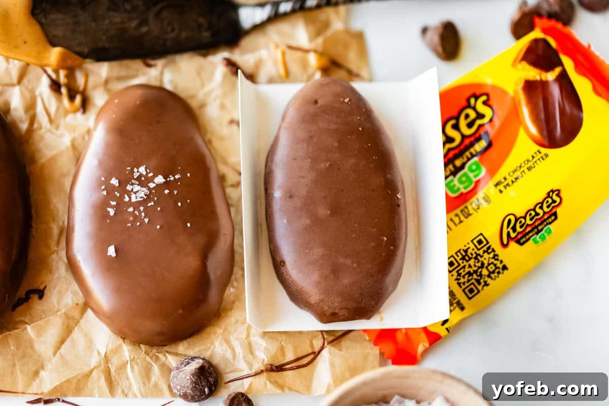 Reese's Easter Peanut Butter Bliss 6 A close-up of two chocolate-covered Reese’s eggs, one sprinkled with sea salt, next to an open yellow Reese’s Egg wrapper on crumpled parchment paper. Chocolate chips and chocolate smudges are nearby.