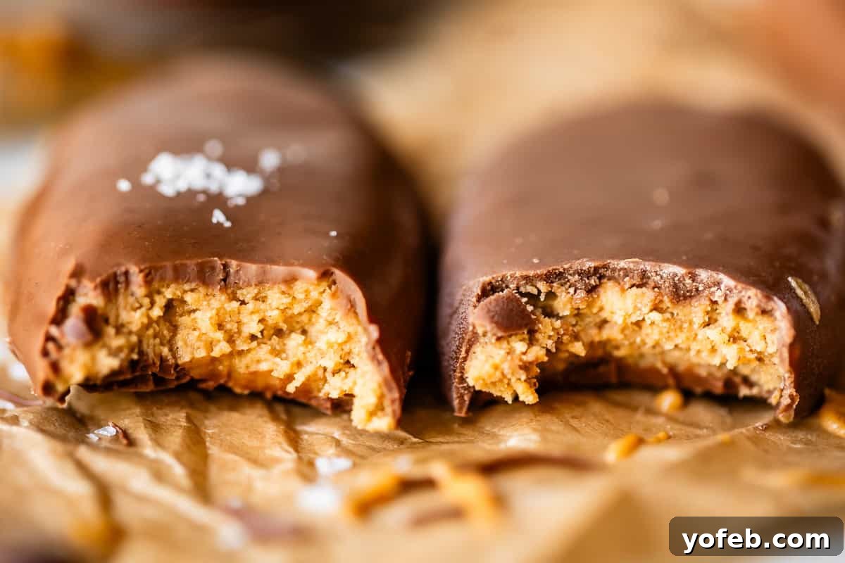 Reese's Easter Peanut Butter Bliss 7 Two chocolate-coated peanut butter bars, each with a bite taken out, revealing a creamy peanut butter filling. They rest on crumpled brown parchment paper, with a sprinkle of salt on one chocolate coating.