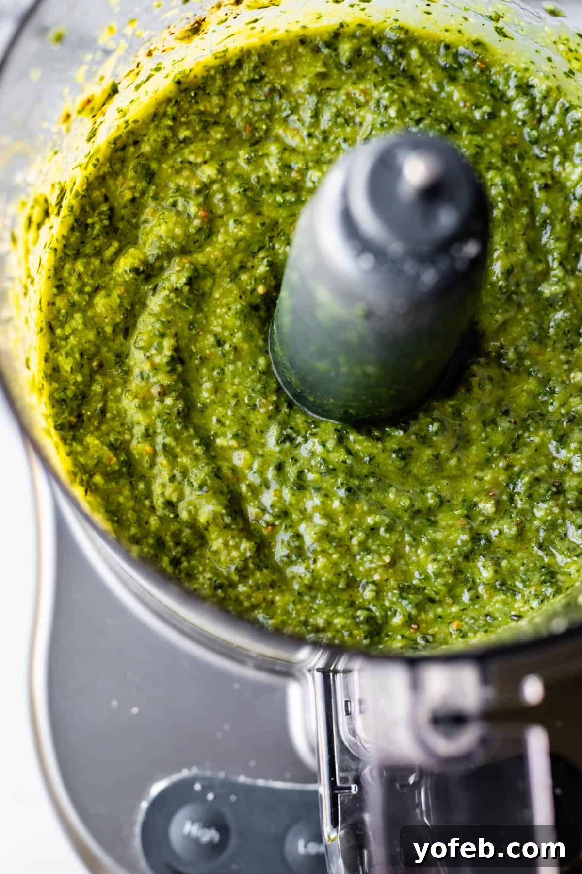 Vibrant Basil Pesto 17 A close-up of vibrant green pesto being blended in a food processor, with the mixture swirling around the central blade and the texture visibly creamy and slightly chunky.