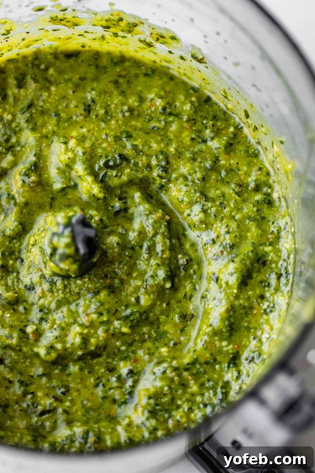Vibrant Basil Pesto 5 A close-up view of vibrant green pesto sauce being blended in a food processor, showing a creamy, textured consistency with visible flecks of herbs and nuts.