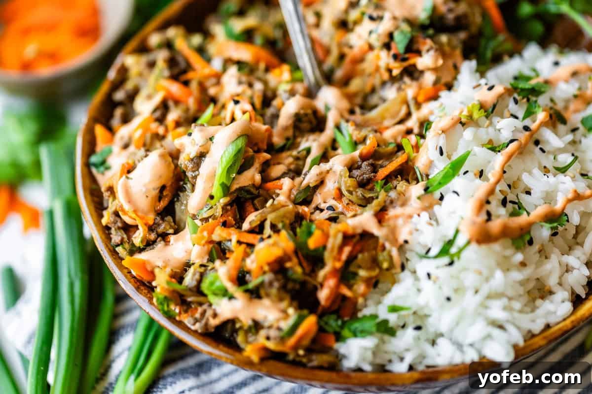 Crispy Egg Roll Bowl: Stir-Fry Recipe Without Wrappers 16 A close-up of a bowl filled with white rice and a colorful mixture of sautéed vegetables, shredded carrots, green onions, and sauce, garnished with a drizzle of creamy dressing. A spoon rests inside the bowl.