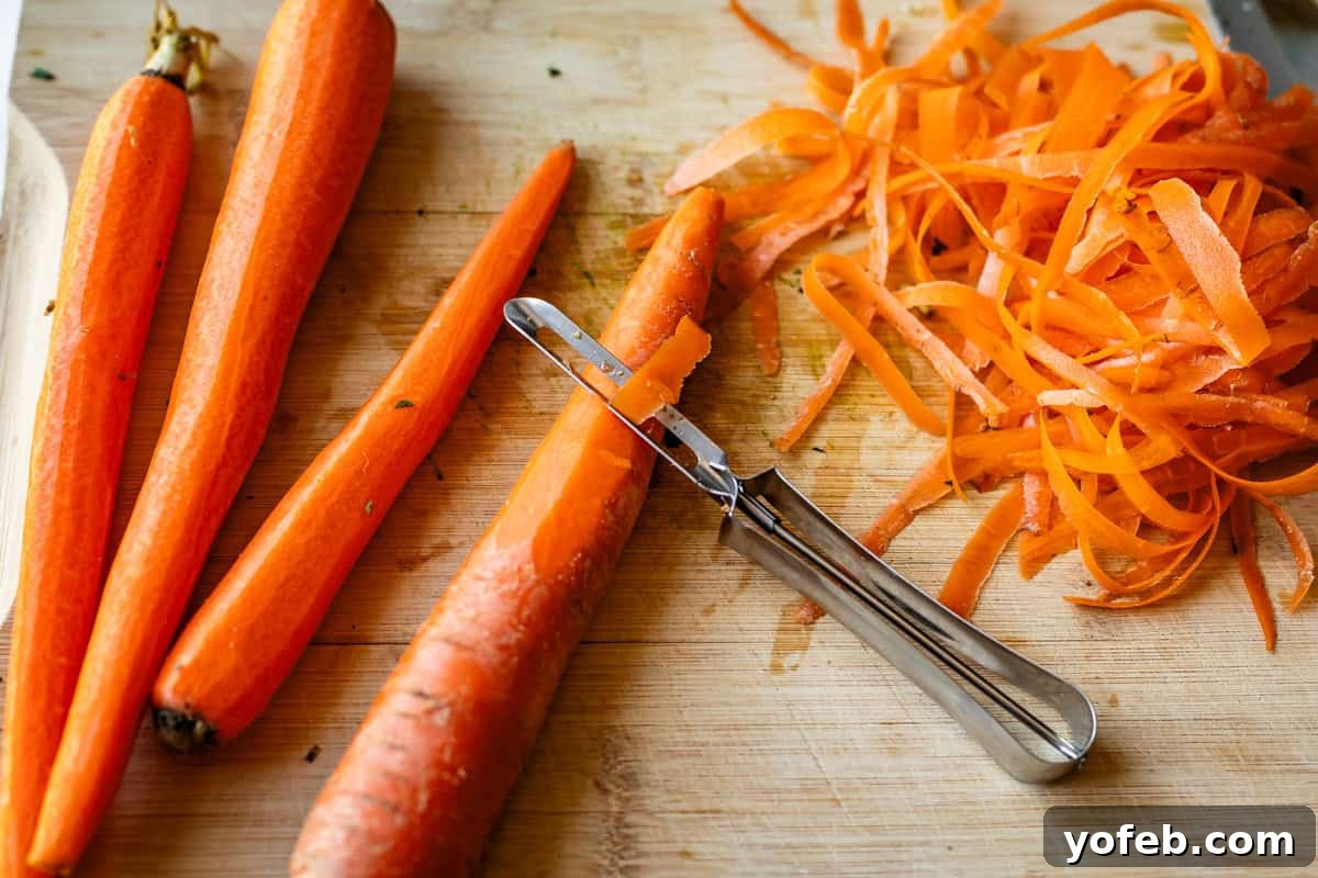 Crispy Egg Roll Bowl: Stir-Fry Recipe Without Wrappers 8 Three whole carrots, a partially peeled carrot with a vegetable peeler, and a pile of carrot peels are on a wooden cutting board.