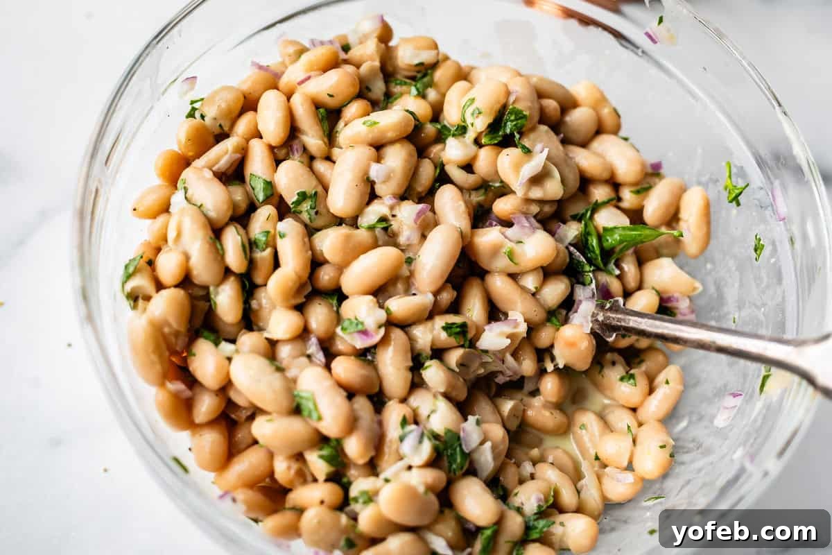 Basil Chicken Salad with Peppery Arugula and Lemon Vinaigrette 6 A clear glass bowl filled with a bean salad made of white beans, chopped red onions, and fresh parsley, with a metal spoon resting inside.