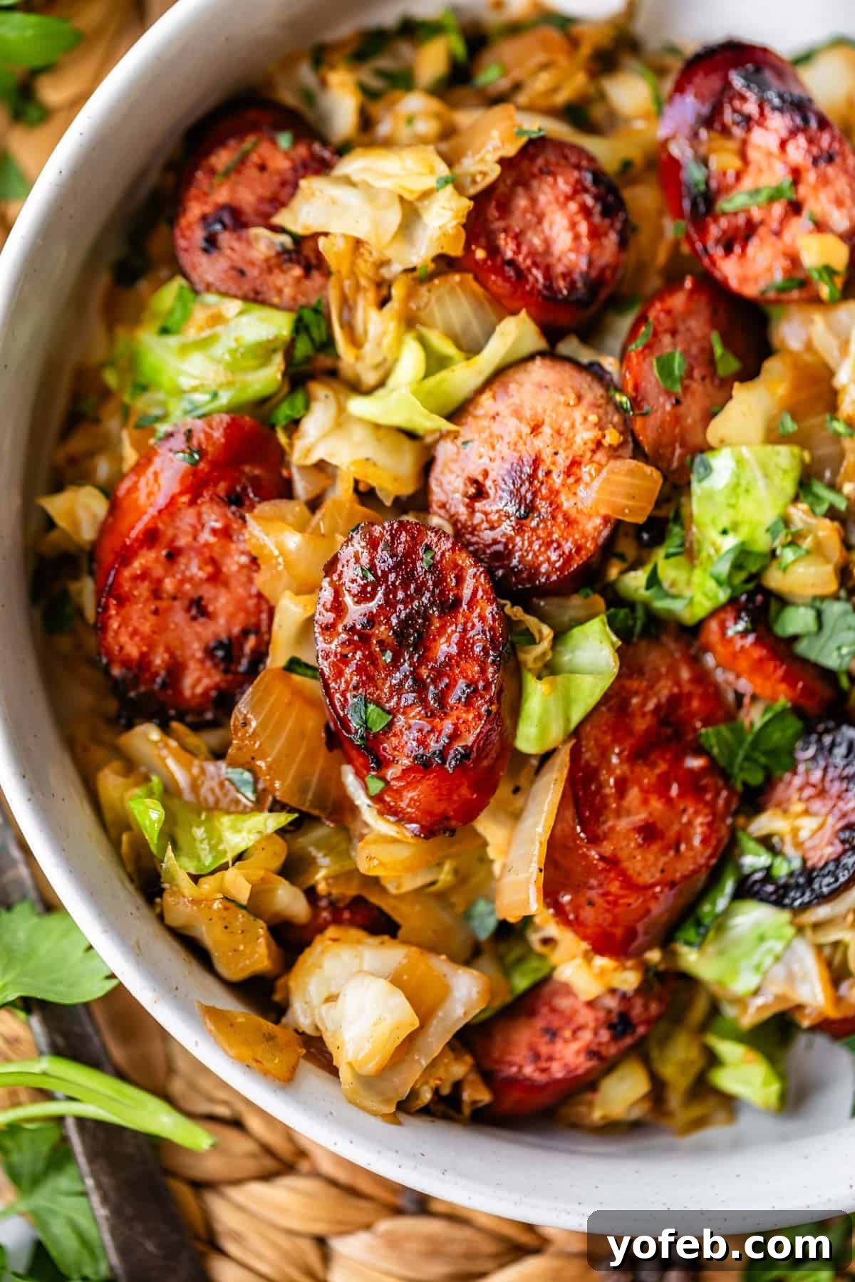 One-Pan Kielbasa and Cabbage Skillet Recipe for Quick Dinners 12 A close-up of a bowl filled with sautéed cabbage, onions, and sliced, browned sausage, garnished with chopped herbs. The dish has a rustic, hearty appearance.