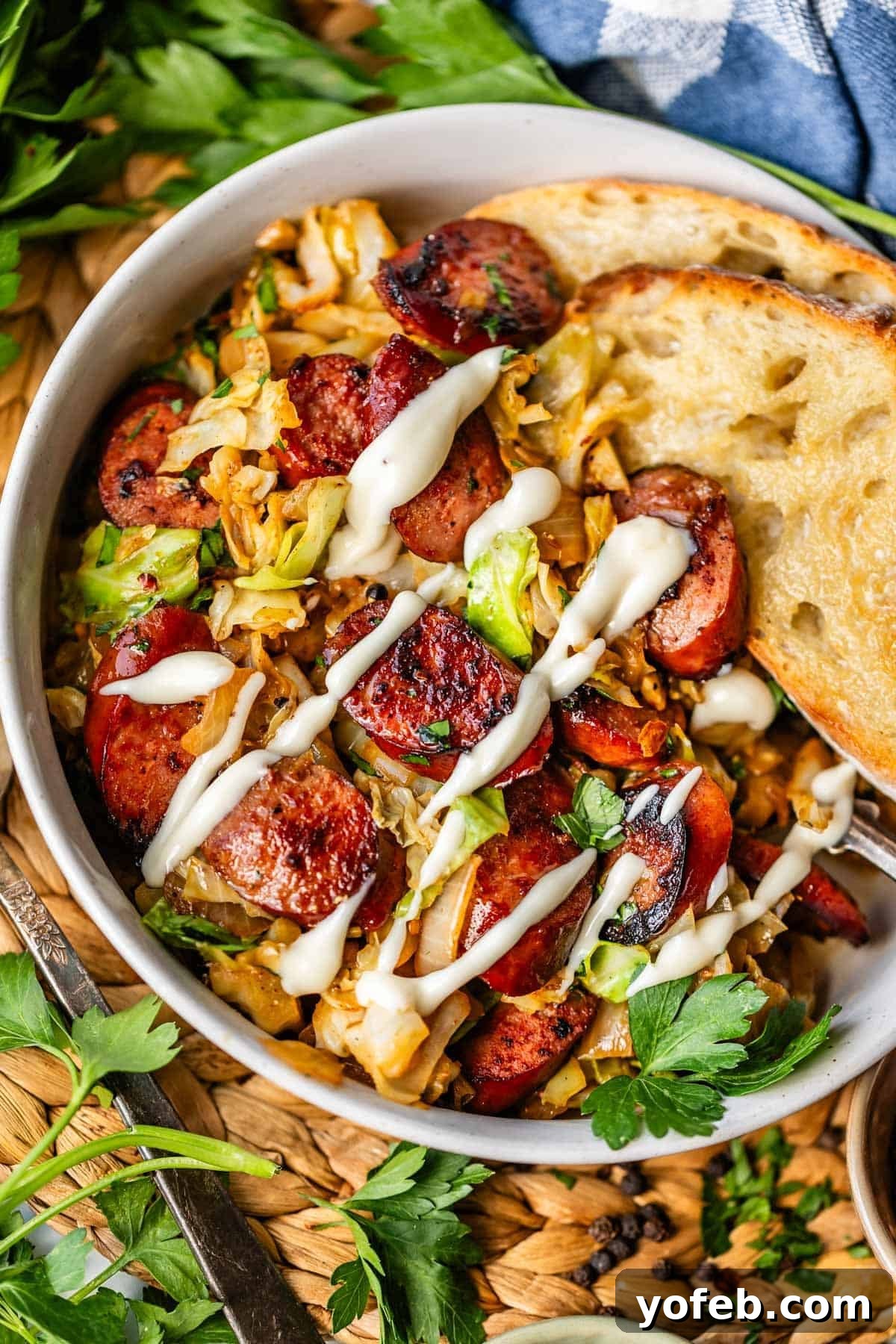 One-Pan Kielbasa and Cabbage Skillet Recipe for Quick Dinners 4 A bowl of sautéed cabbage and sliced sausage, topped with a drizzle of creamy white sauce, served with two slices of toasted bread and garnished with fresh parsley.