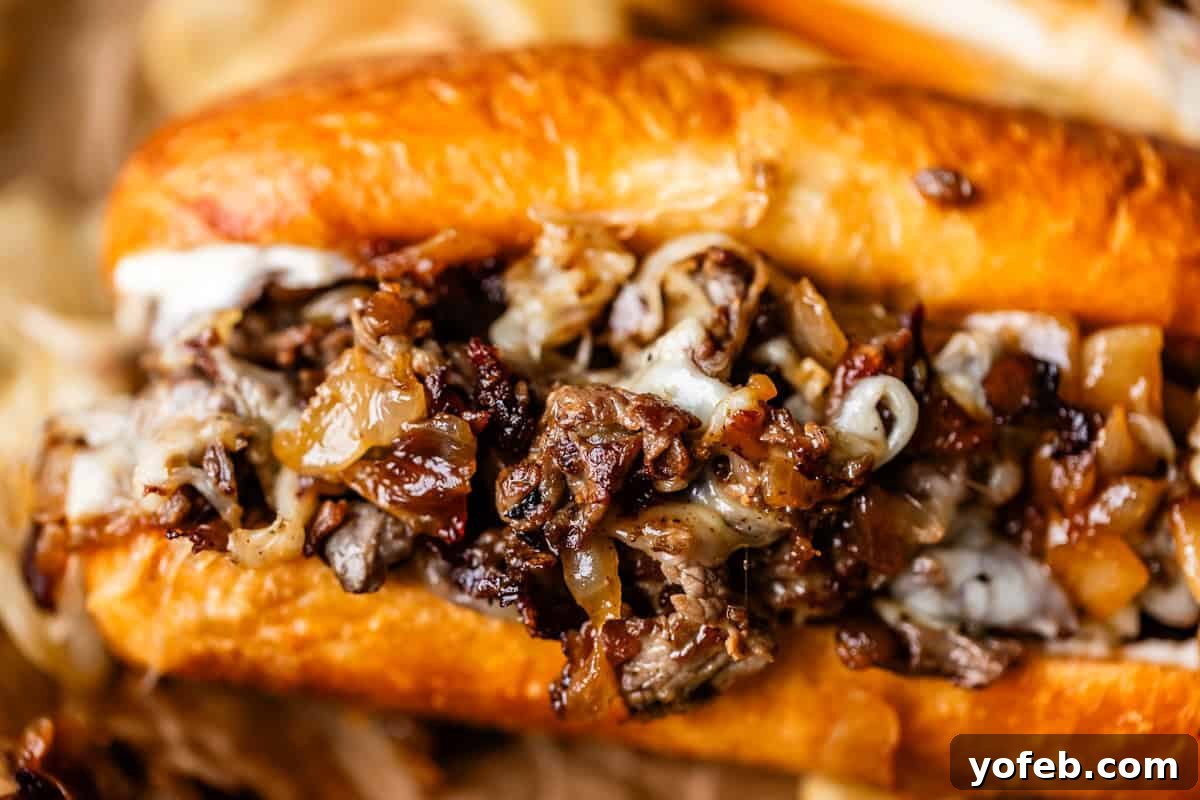 Authentic Philly Cheesesteak Recipe: How to Make It at Home 4 Close-up of a Philly cheesesteak sandwich filled with sliced beef, melted cheese, and sautéed onions in a toasted hoagie roll.