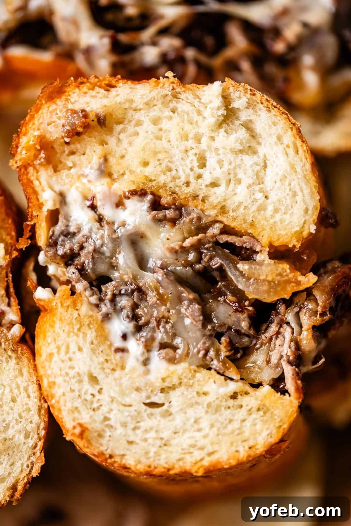 Authentic Philly Cheesesteak Recipe: How to Make It at Home 5 A close-up of a sandwich with golden, crusty bread filled with melted cheese, thinly sliced beef, and creamy sauce.