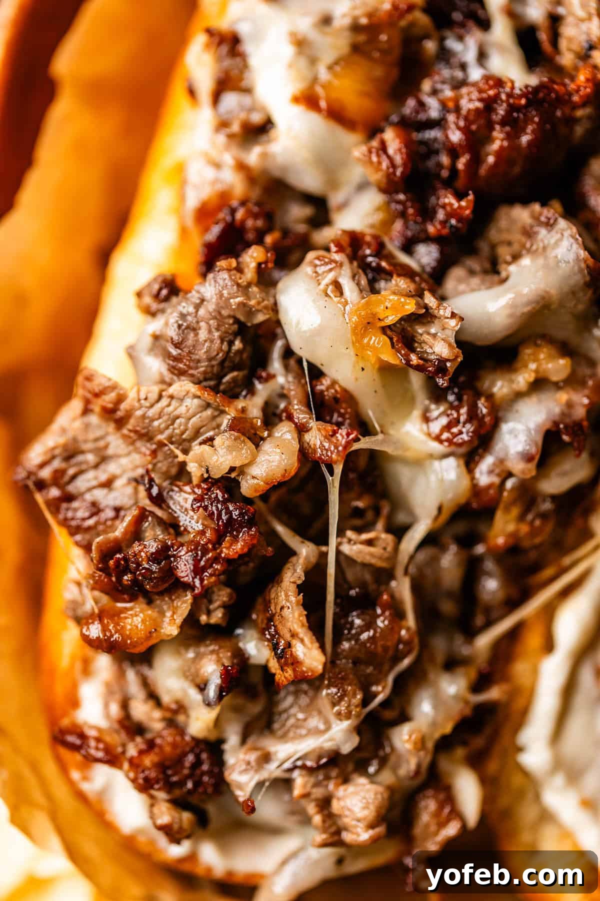 Authentic Philly Cheesesteak Recipe: How to Make It at Home 6 Close-up of a Philly cheesesteak sandwich with melted cheese, grilled steak slices, and caramelized onions on a toasted hoagie roll.
