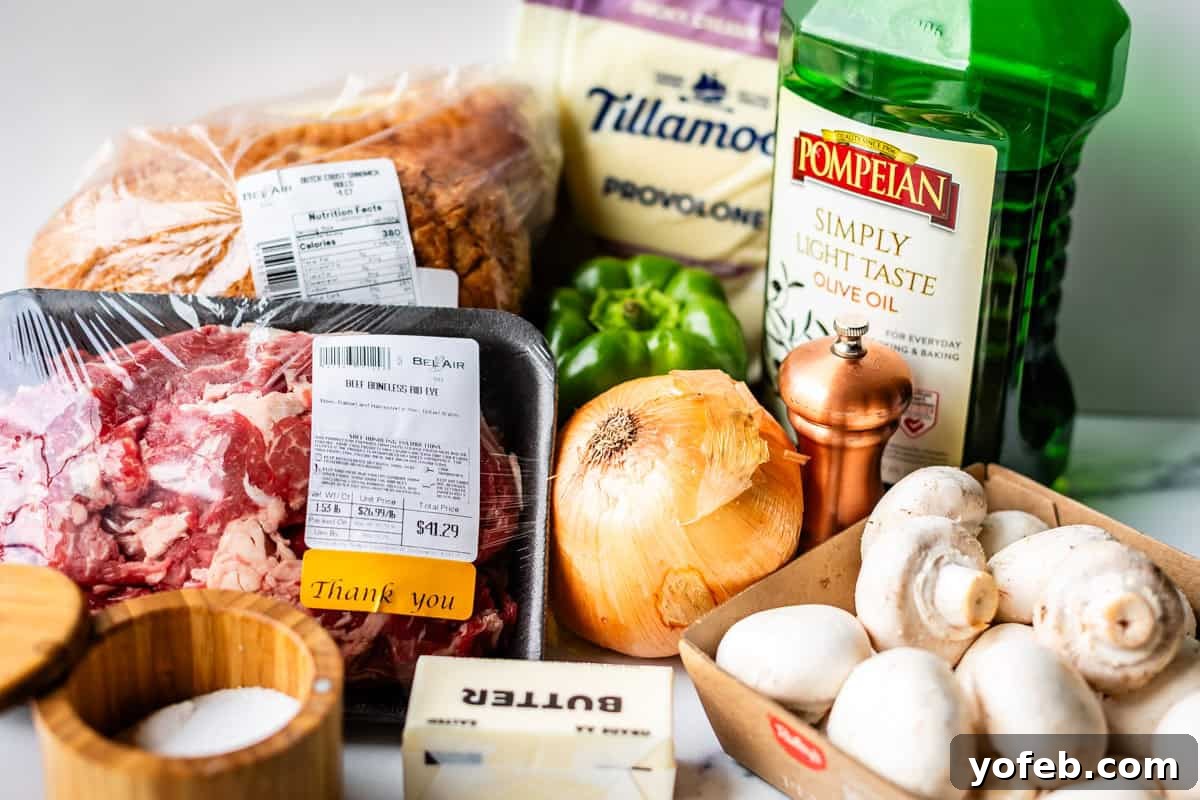 Authentic Philly Cheesesteak Recipe: How to Make It at Home 7 A variety of fresh ingredients on a counter, including sliced bread, provolone cheese, olive oil, beef, green bell pepper, an onion, mushrooms, butter, salt, and a pepper grinder.