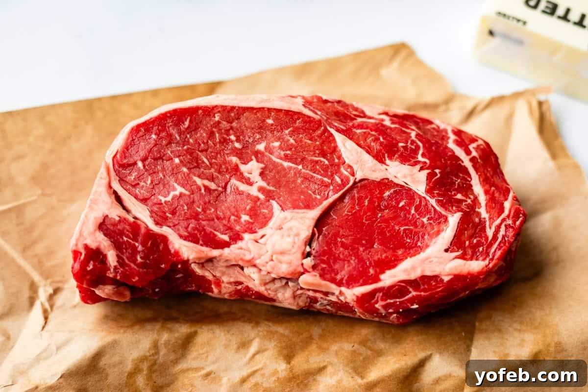 Authentic Philly Cheesesteak Recipe: How to Make It at Home 8 A raw ribeye steak with marbling of fat sits on a piece of brown butcher paper, with part of a stick of butter visible in the background.