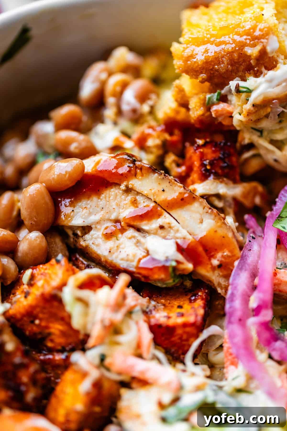 Smoky BBQ Chicken Rice Bowls with Grilled Veggies 4 Close-up of a vibrant dish featuring grilled chicken slices, barbecue sauce, baked beans, cornbread, coleslaw, pickled red onions, and roasted sweet potatoes, all mixed together for a colorful and hearty meal.