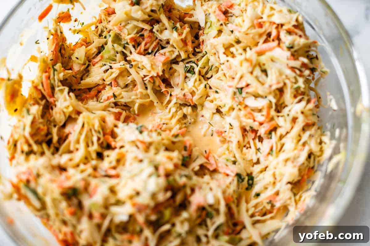 Classic Creamy Coleslaw Recipe with Tangy Dressing 11 A close-up of a glass bowl filled with creamy coleslaw, featuring shredded cabbage, carrots, and herbs mixed with a dressing.