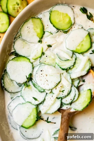 Classic Creamy Coleslaw Recipe with Tangy Dressing 17 creamy cucumber salad with onions and thyme in a white bowl with wooden spoon.